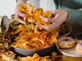 Tafel vol vet eten. Vrouw graait in een bak chips.